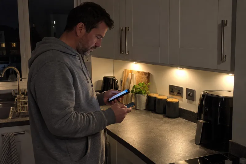 Man paying a deposit on his phone at the kitchen counter at night